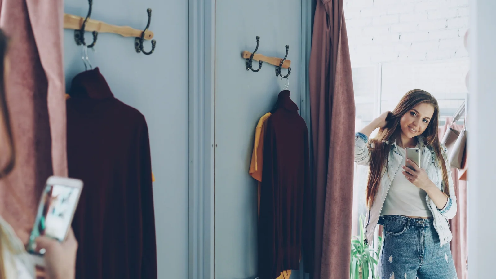 Femme en cabine d'essayage entourée de vêtements